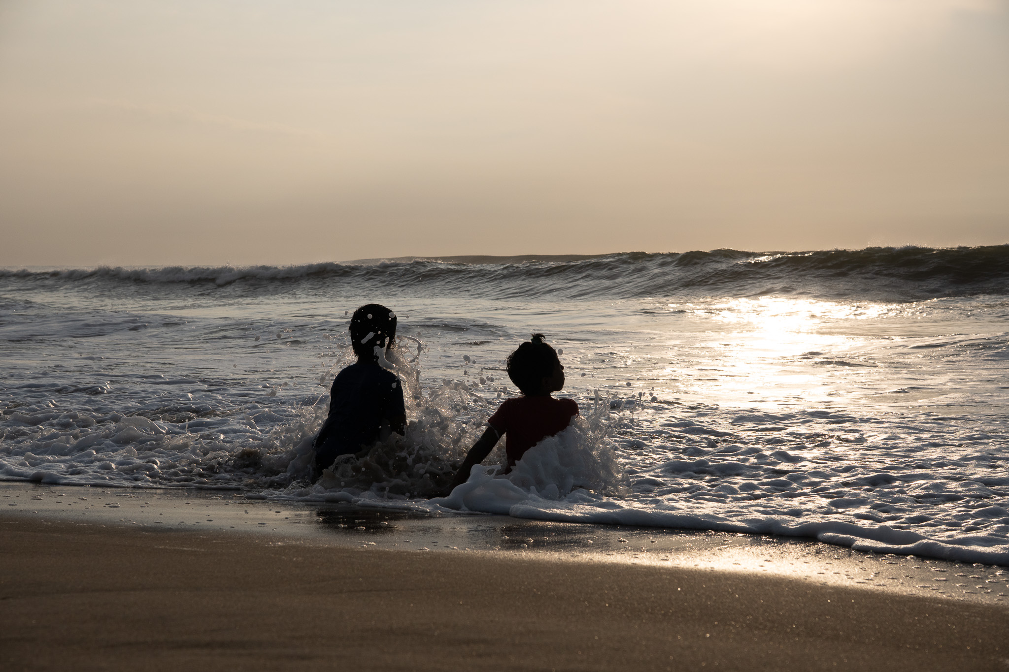 two kids playing in the ocean waves at sunset